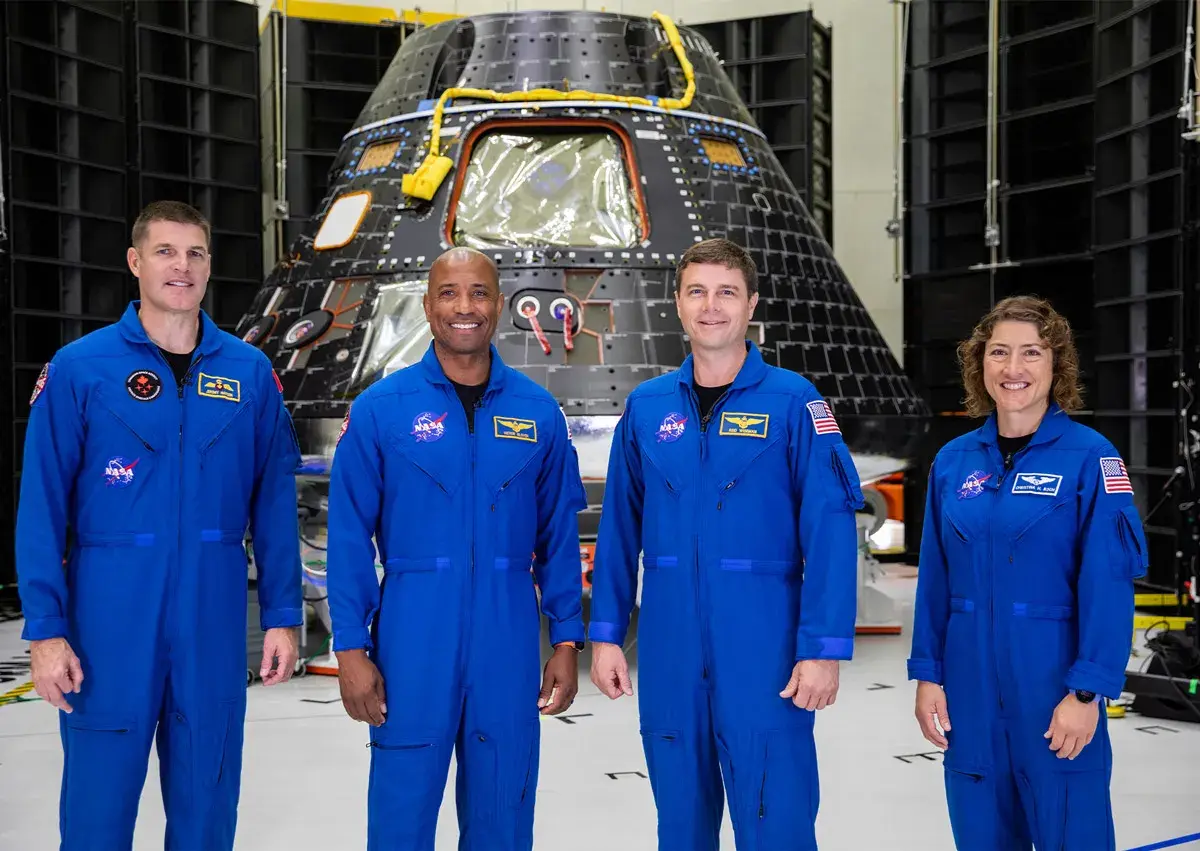 تیم 4 نفره مأموریت آرتمیس 2 ناسا در مرکز فضایی کندی با لباس‌های کار آبی یکپارچه ایستاده‌اند و به دوربین لبخند می‌زنند.